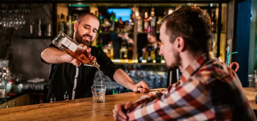 male bartender pouring drink into rocks glass