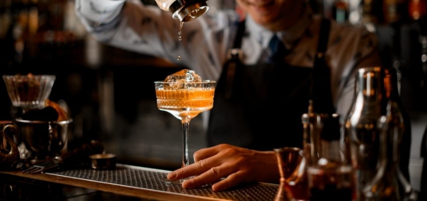 cocktail being poured into glass from shaker by bartender