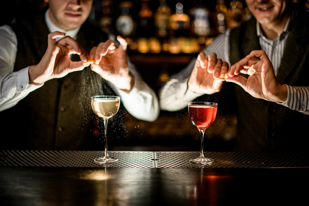 two bartenders squeezing lime juice on top of cocktail on bar rail